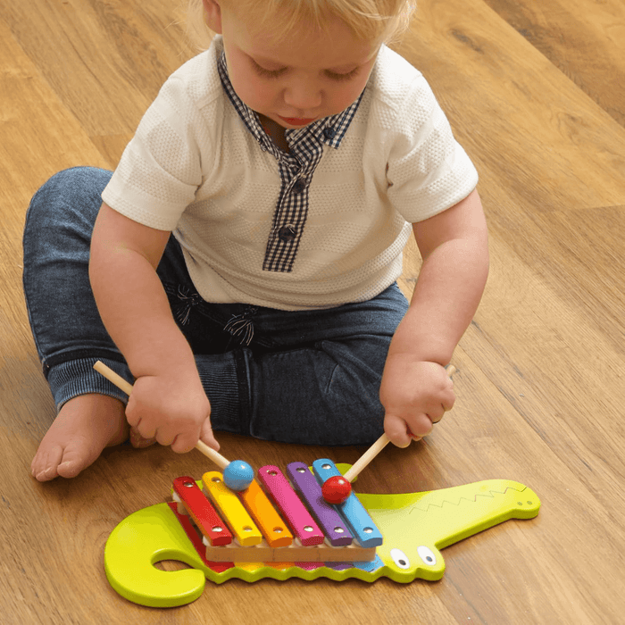 small toddle boy plays with the musical crocodile on wooden floor