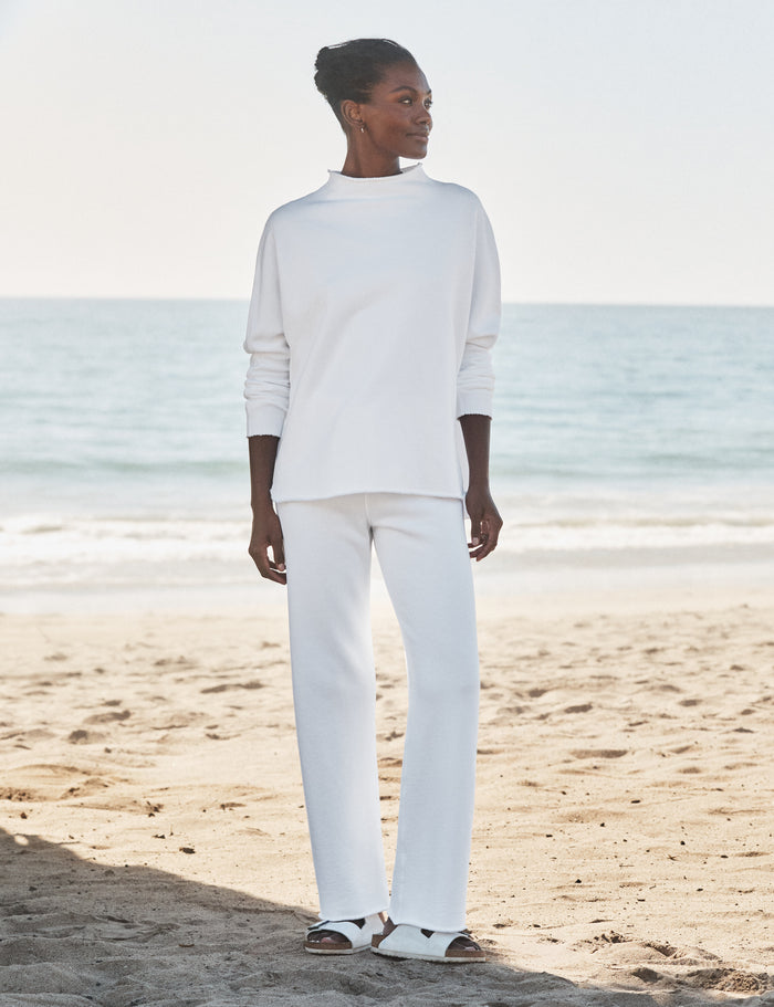 Person wearing a white outfit standing on a beach with ocean in the background