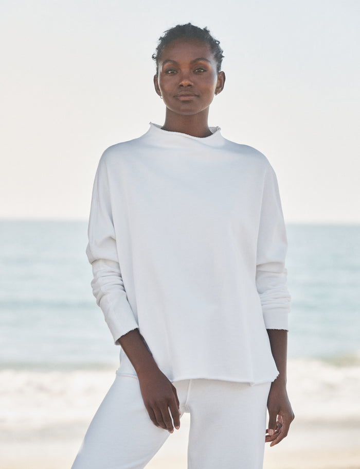 Person wearing a white outfit standing on a beach with ocean in the background
