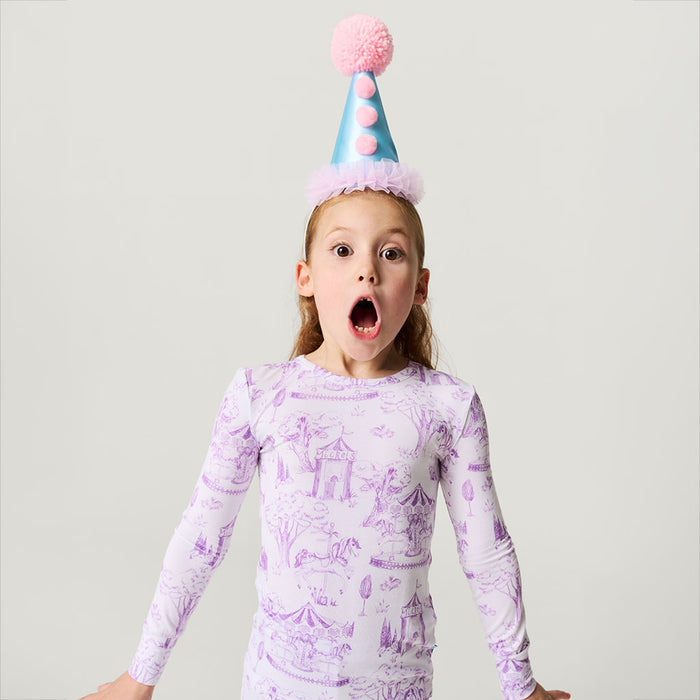 Child wearing a purple long-sleeve shirt with a carousel design and a colorful party hat.