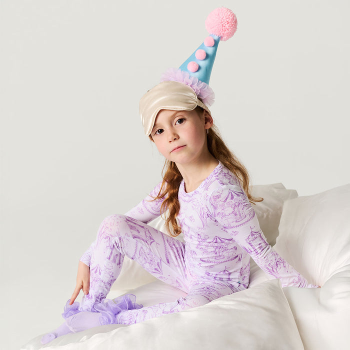 Child wearing a purple dinosaur-themed onesie and a colorful party hat on a white background