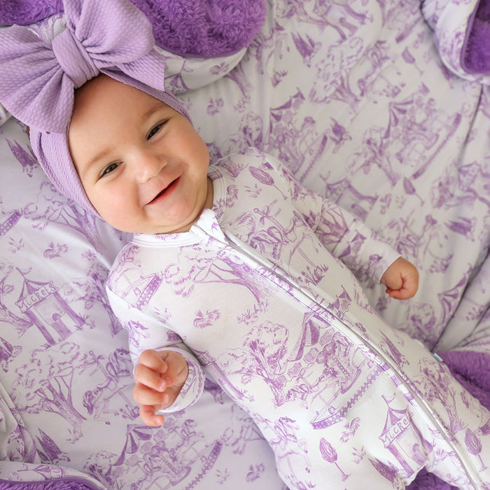 Baby in a purple and white patterned outfit with matching headband on a matching blanket.