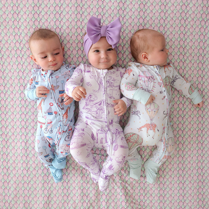 Three babies in patterned onesies on a pink and green checkered background