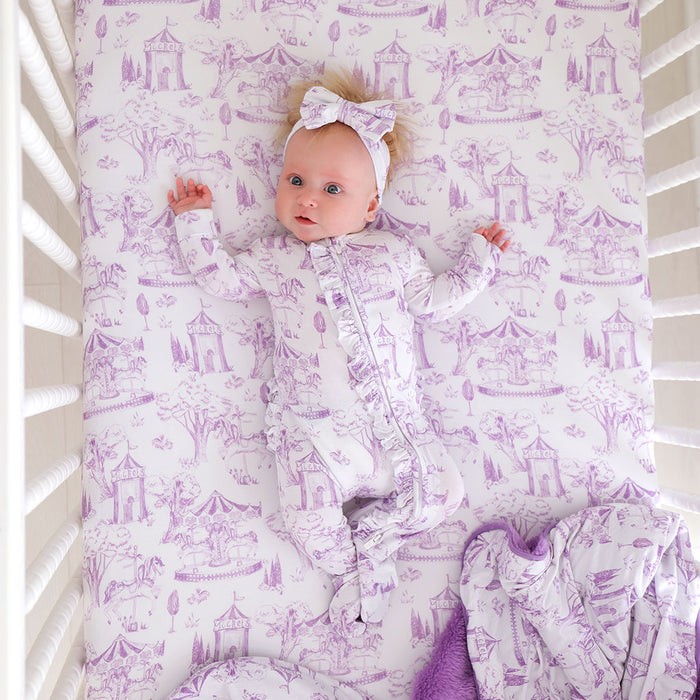 Baby lying in a crib with purple and white patterned bedding