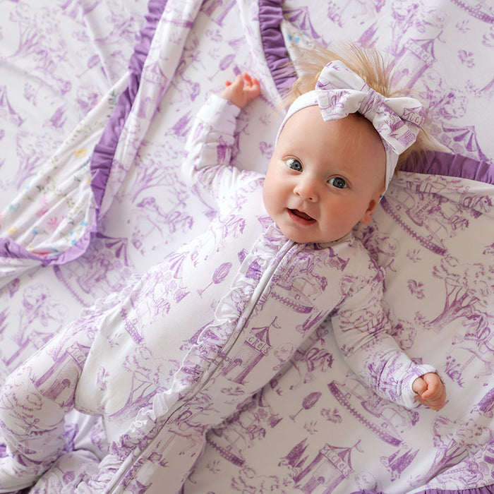 Baby in a purple and white patterned outfit lying on a matching blanket