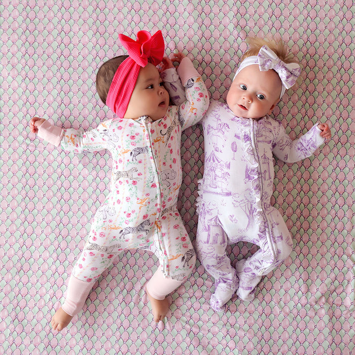 Two dolls wearing patterned one pieces and headbands on a pink and green textured background