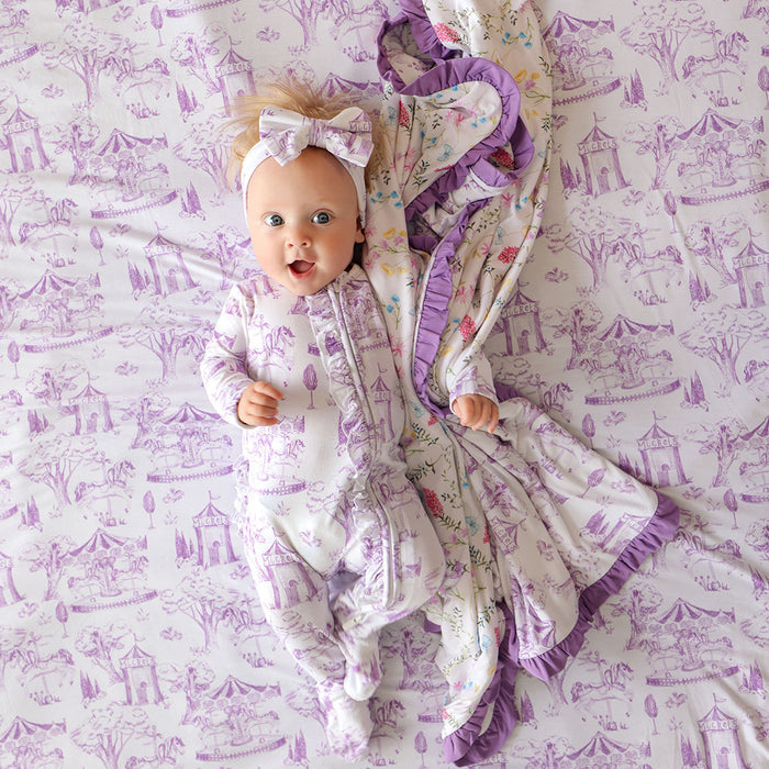 Baby in a purple and white outfit with a matching blanket on a patterned surface