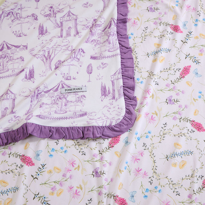Close up image of blanket with purple carnival print with reversible floral print.