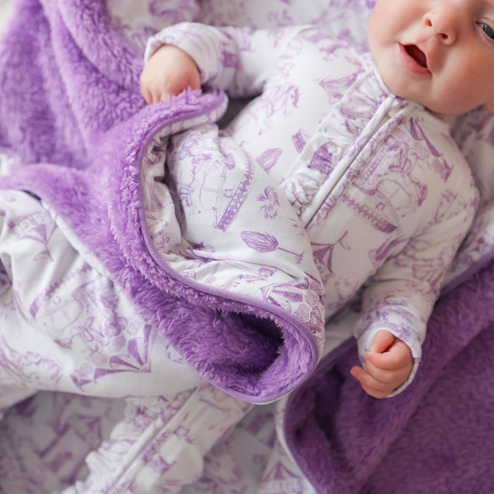 Baby in a purple and white patterned outfit lying on a purple blanket