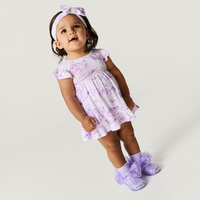 Baby wearing a purple floral dress and matching shoes on a light gray background