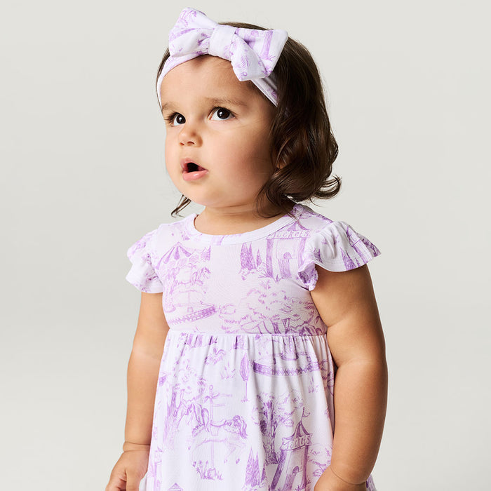 Baby wearing a purple and white dress with a matching headband against a plain background