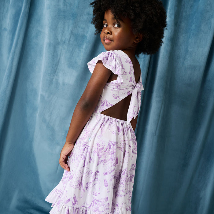 Child wearing a white dress with purple floral patterns against a blue curtain background