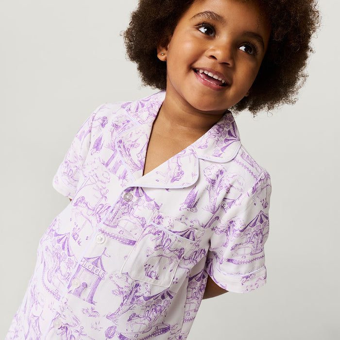 Child wearing a purple and white patterned pajama shirt on a plain background