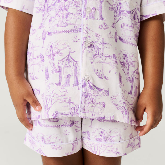 Child wearing a purple and white pajama set with a carousel design on a plain background