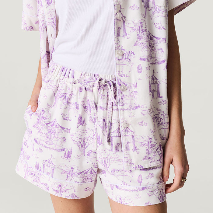 Person wearing a white shirt and purple patterned shorts on a plain background