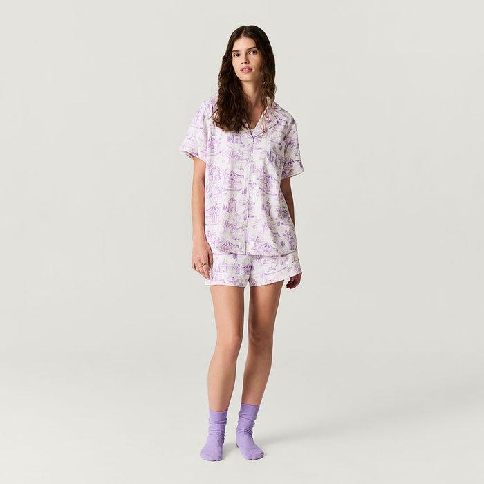 Woman wearing a light purple pajama set with a floral pattern on a plain background