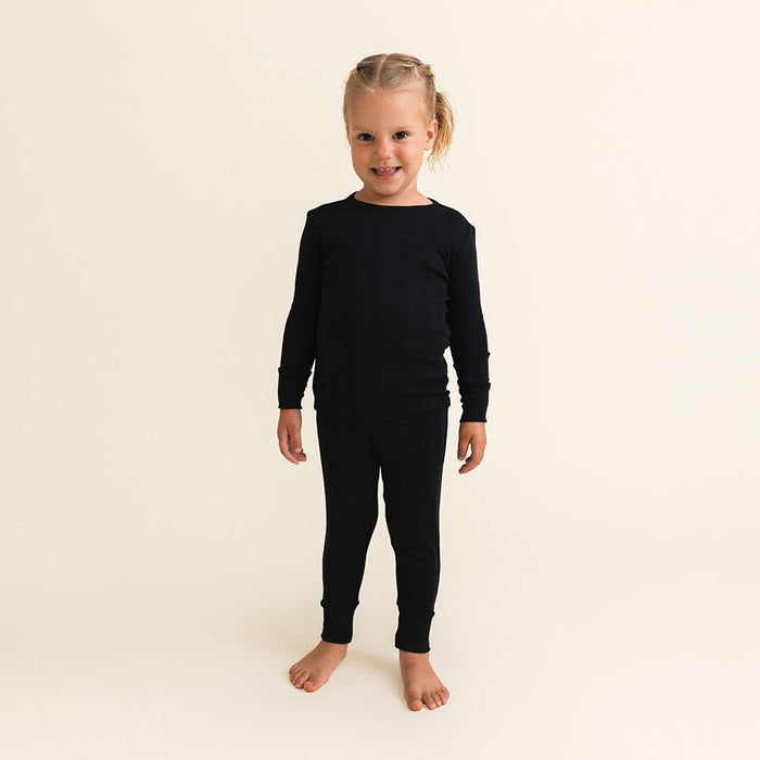 Child wearing black long-sleeve shirt and pants pajama set on a beige background