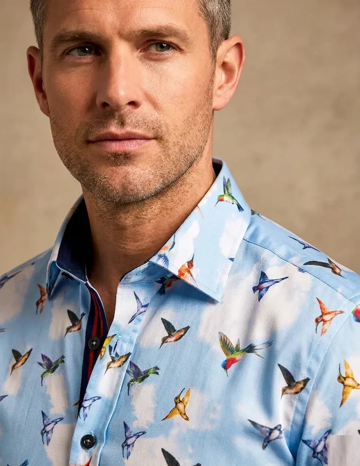 Man wearing a light blue shirt with colorful bird pattern against a beige background