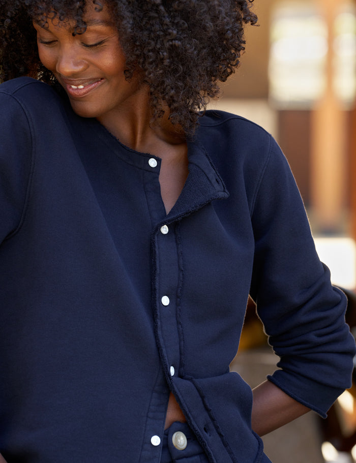 A close-up of a woman wearing a navy blue cardigan with a soft collar, shown in a warm, softly blurred outdoor setting.