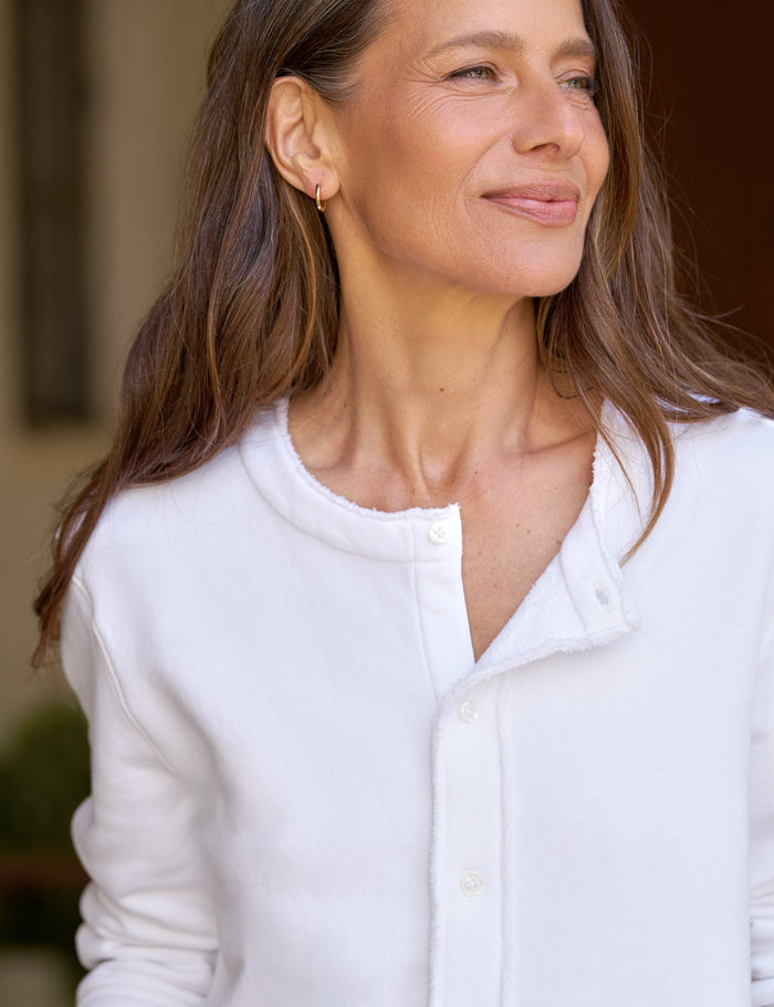 A close-up shot of a woman wearing a white cardigan, set against a softly blurred background.
