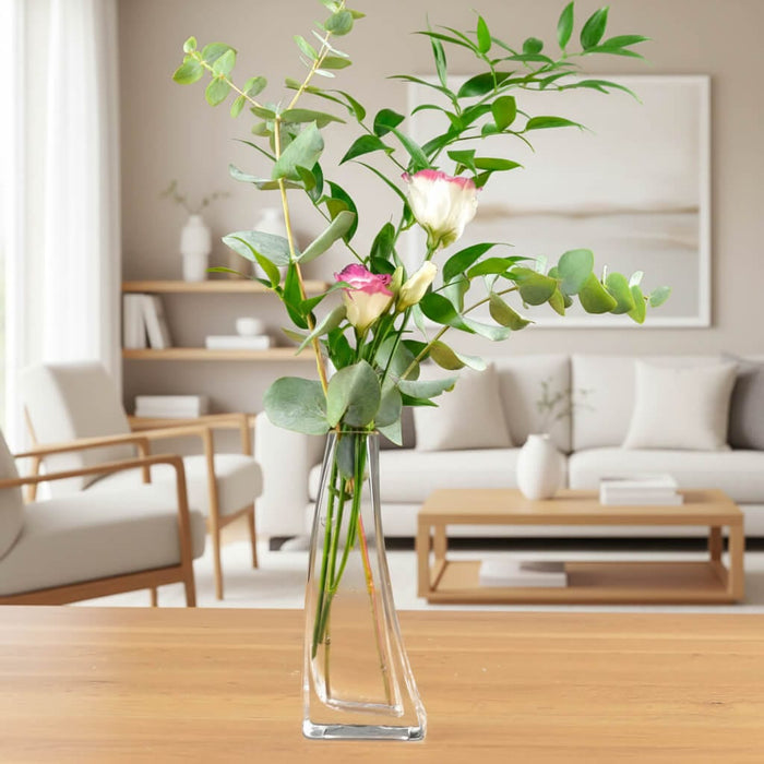 Curved glass vase of flowers and eucalyptus branches on a wooden table in a living room