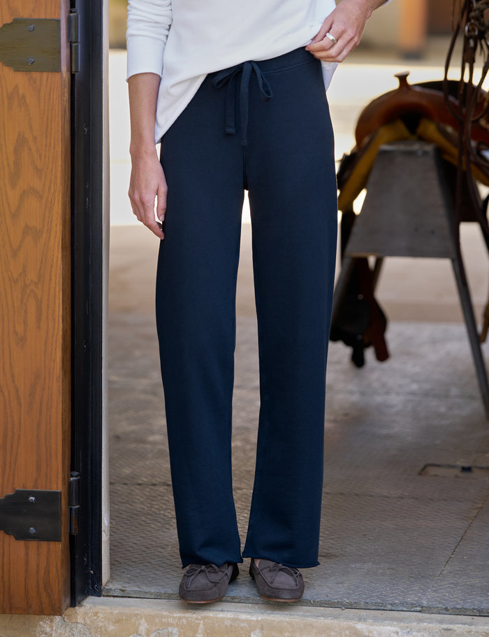A person wearing dark navy wide-leg drawstring pants, a white long-sleeve top, and brown shoes, standing in a doorway.
