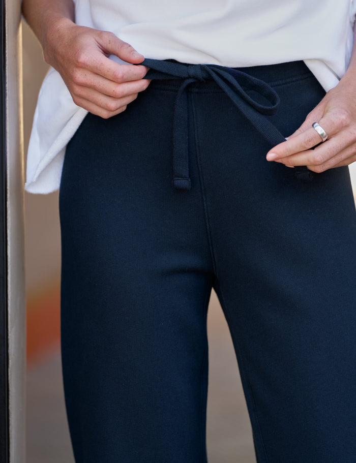 Close-up of a person wearing dark navy drawstring sweatpants and a white top, with hands adjusting the waistband and a ring visible on one finger.