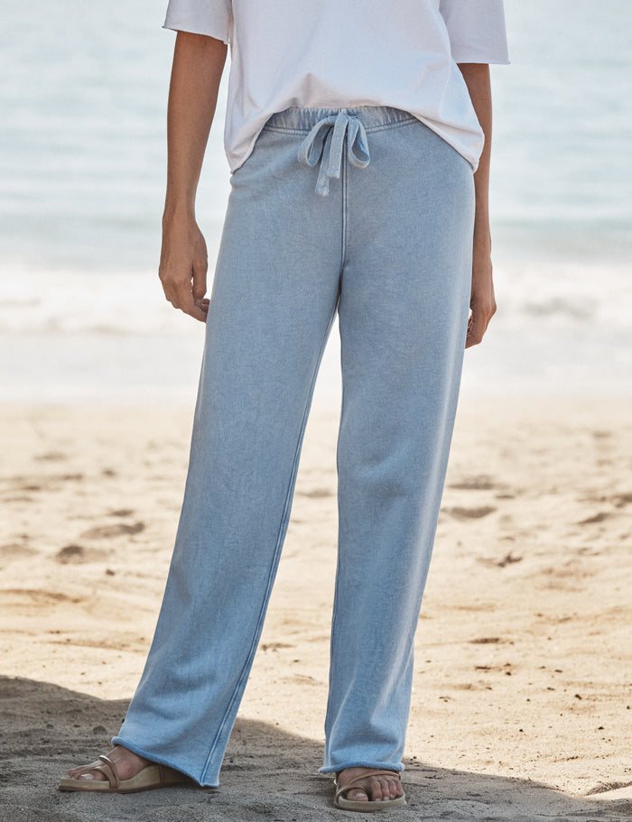 Person wearing light blue pants and a white top on a beach.