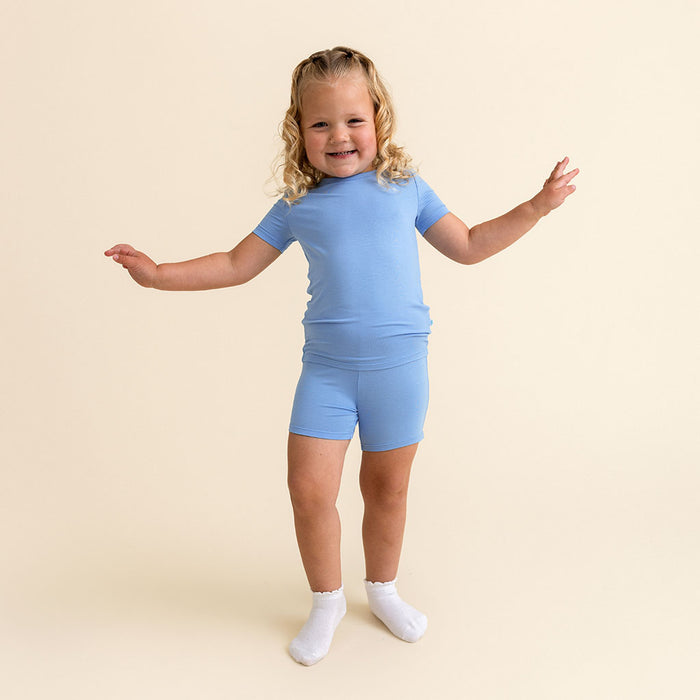 Girl standing, smiling and playing, wearing the Posh Peanut Chatham Blue Classic Pajama Short Set.