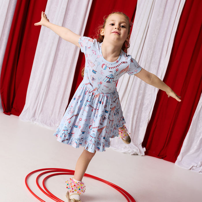 Young girl in a patterned dress standing on a red circle with curtains in the background
