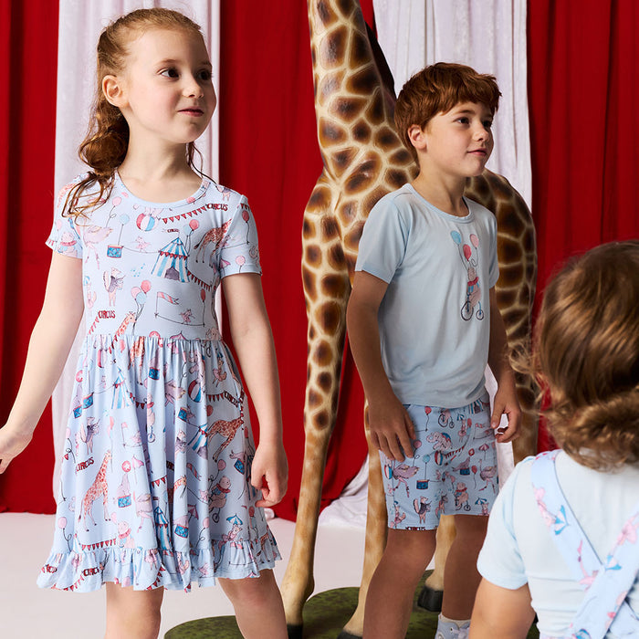 3 children wearing matching circus printed outfits standing against a red and white curtain