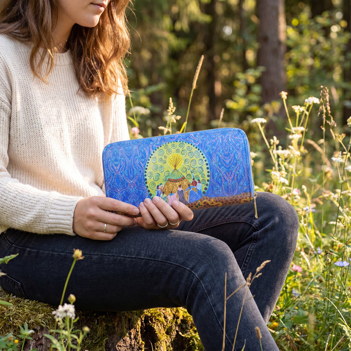 Person holding a blue clutch with a colorful design in a natural setting