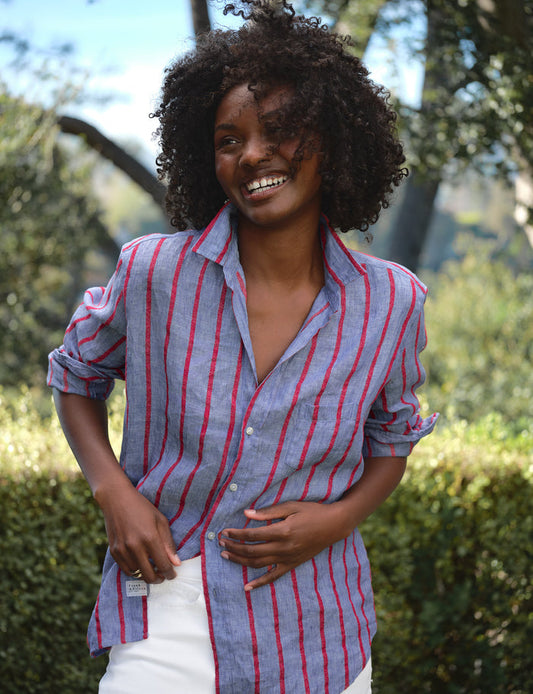Woman wearing a blue and red striped shirt outdoors with greenery in the background