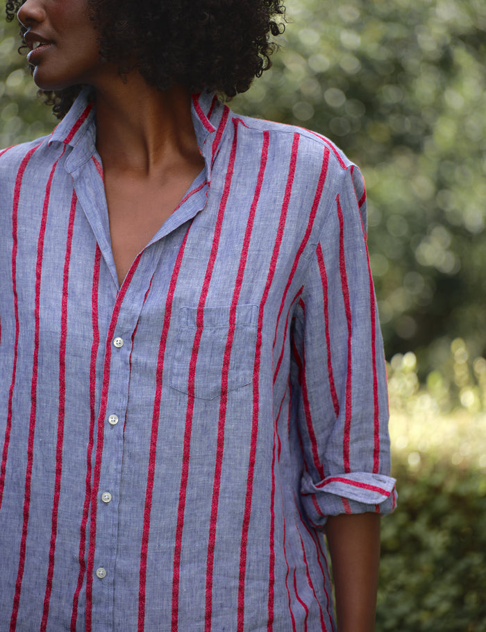Person wearing a blue and red striped shirt with a blurred natural background