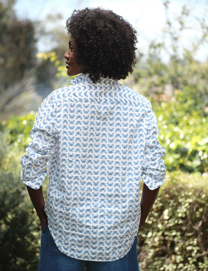 Person wearing a patterned shirt standing outdoors with greenery in the background