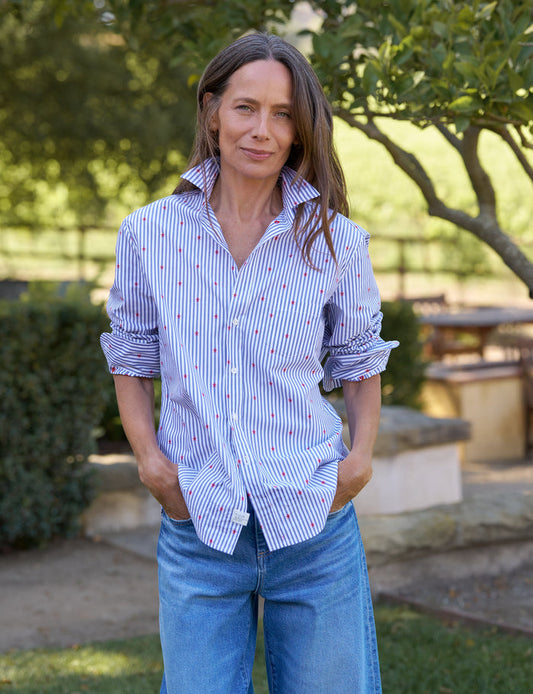 Woman wearing a striped shirt and jeans standing outdoors with greenery in the background