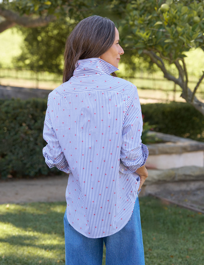 Woman wearing a blue and white striped shirt with red dots outdoors.