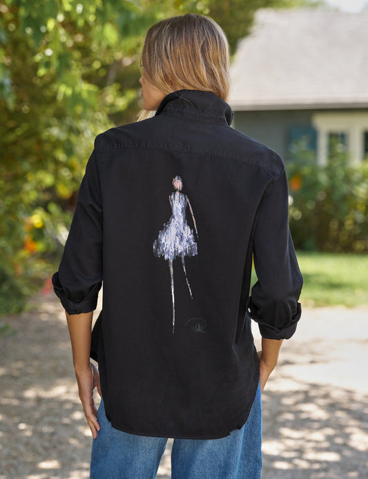 Person wearing a black shirt with a white graphic on the back, standing outdoors.