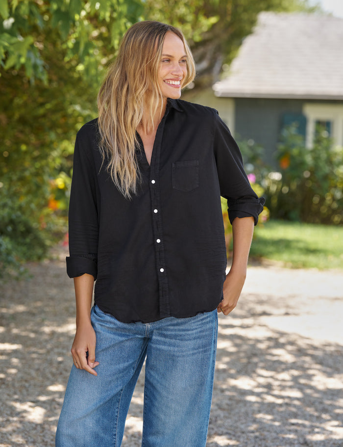 Woman wearing a black shirt and blue jeans standing outdoors.
