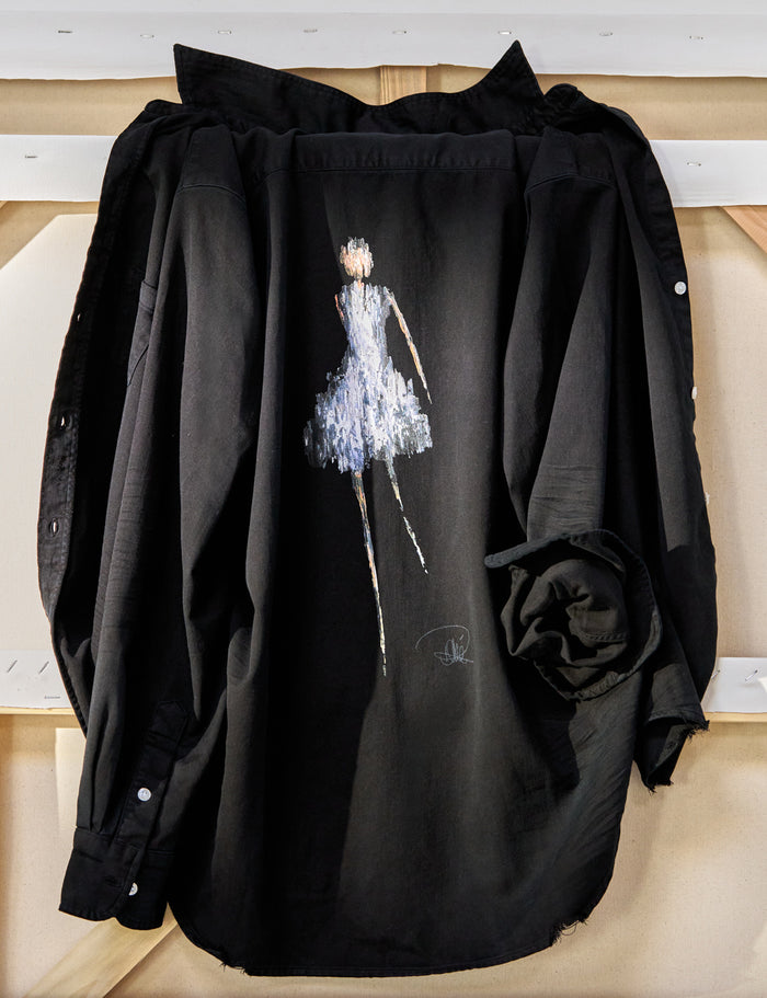 Black shirt with a graphic of a dancer in a blue dress on a wooden surface