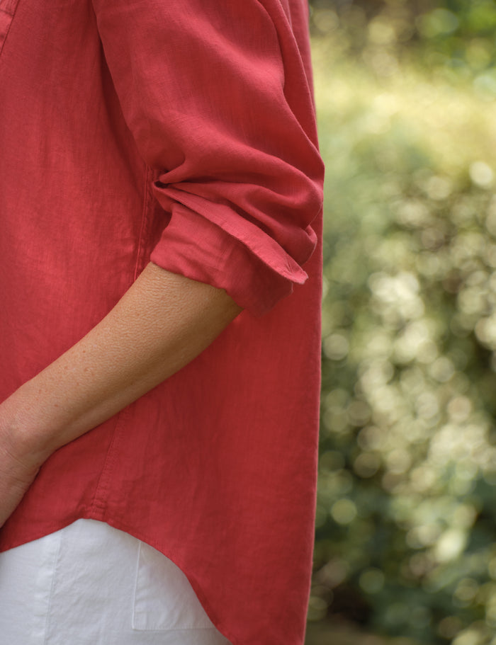 Person wearing a red shirt with rolled-up sleeves against a blurred green background