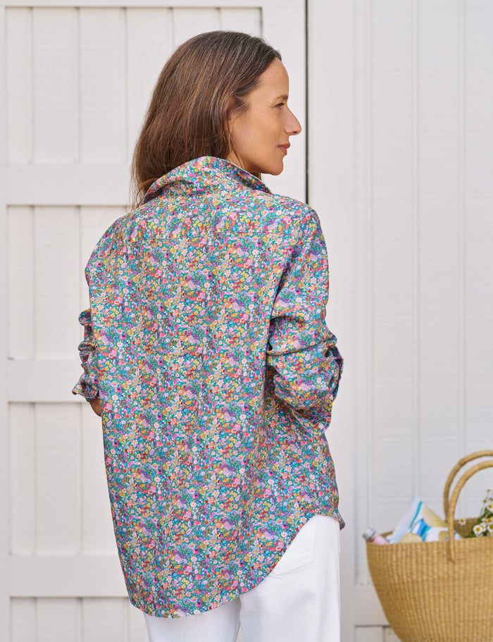 Woman wearing a colorful floral shirt standing against a white wooden background