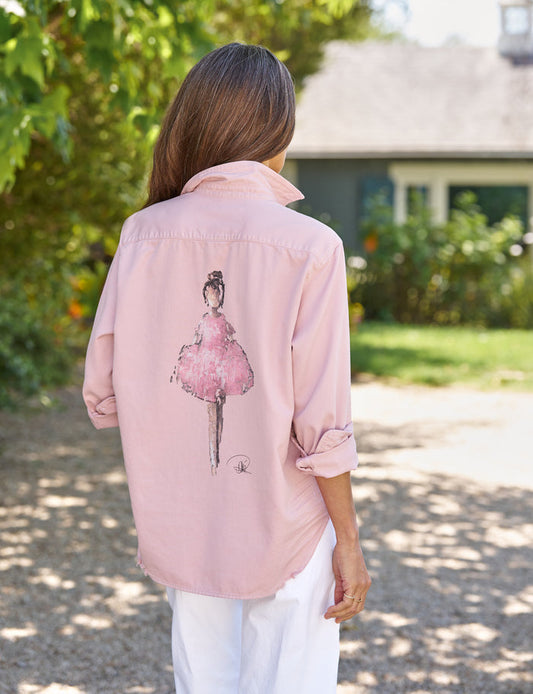 Person wearing a pink shirt with a graphic of a ballerina outdoors.