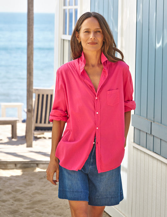 Woman wearing a bright pink shirt and blue shorts standing on a beach.