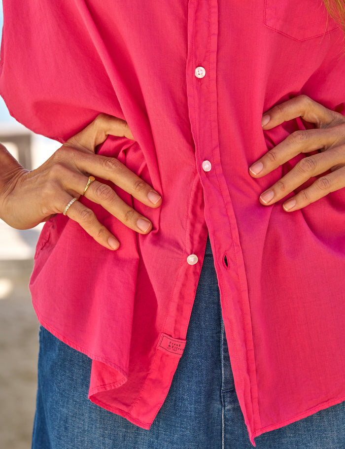 Person wearing a bright pink button-up shirt with blue jeans, hands on hips.