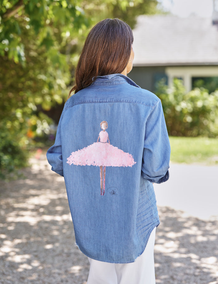 Person wearing a denim shirt with a pink ballerina design outdoors.