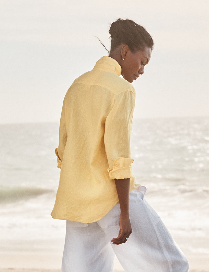 Person wearing a yellow shirt and white pants walking on a beach.