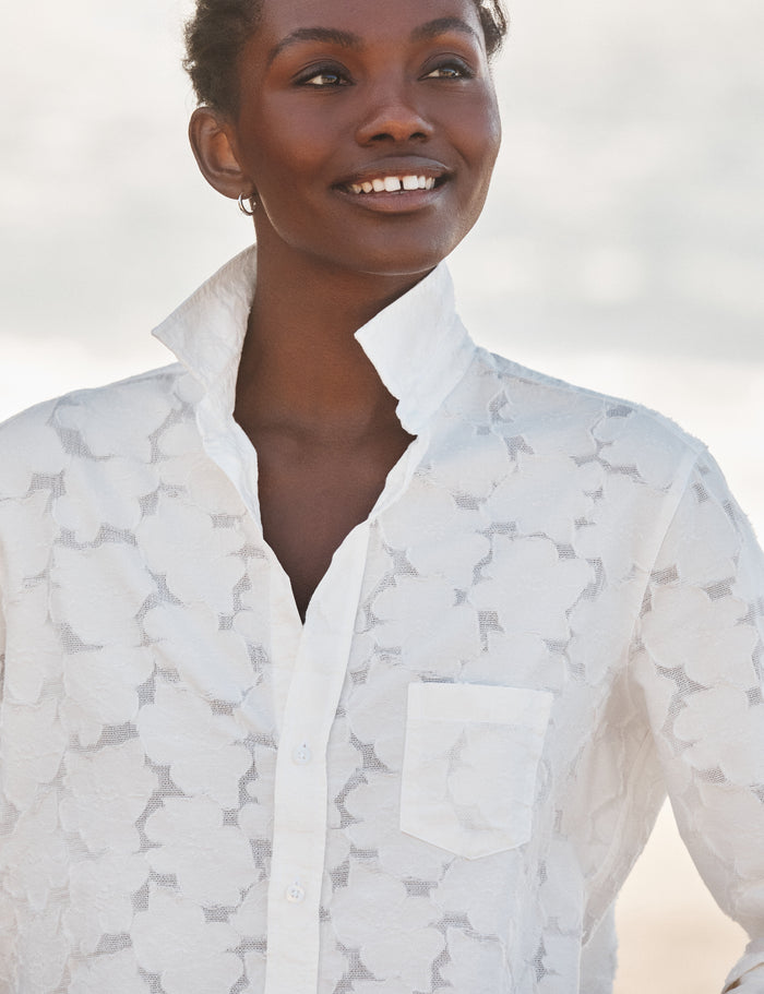 Woman wearing a white patterned shirt against a blurred natural background