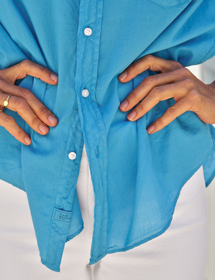 Close-up of a blue shirt with hands adjusting it on a white background