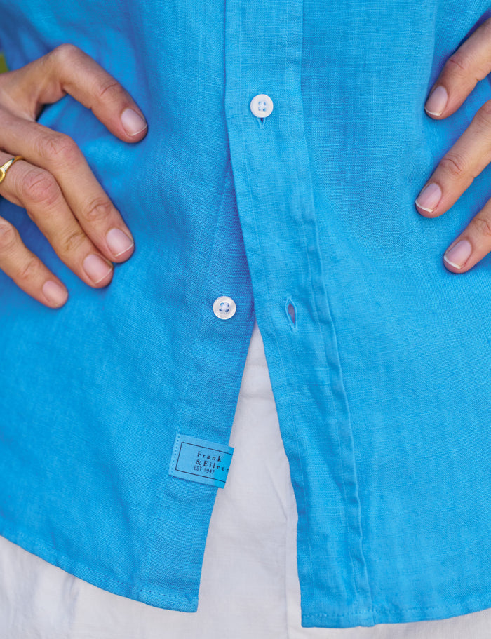 Close-up of a blue shirt with a brand label, showing hands adjusting the collar.